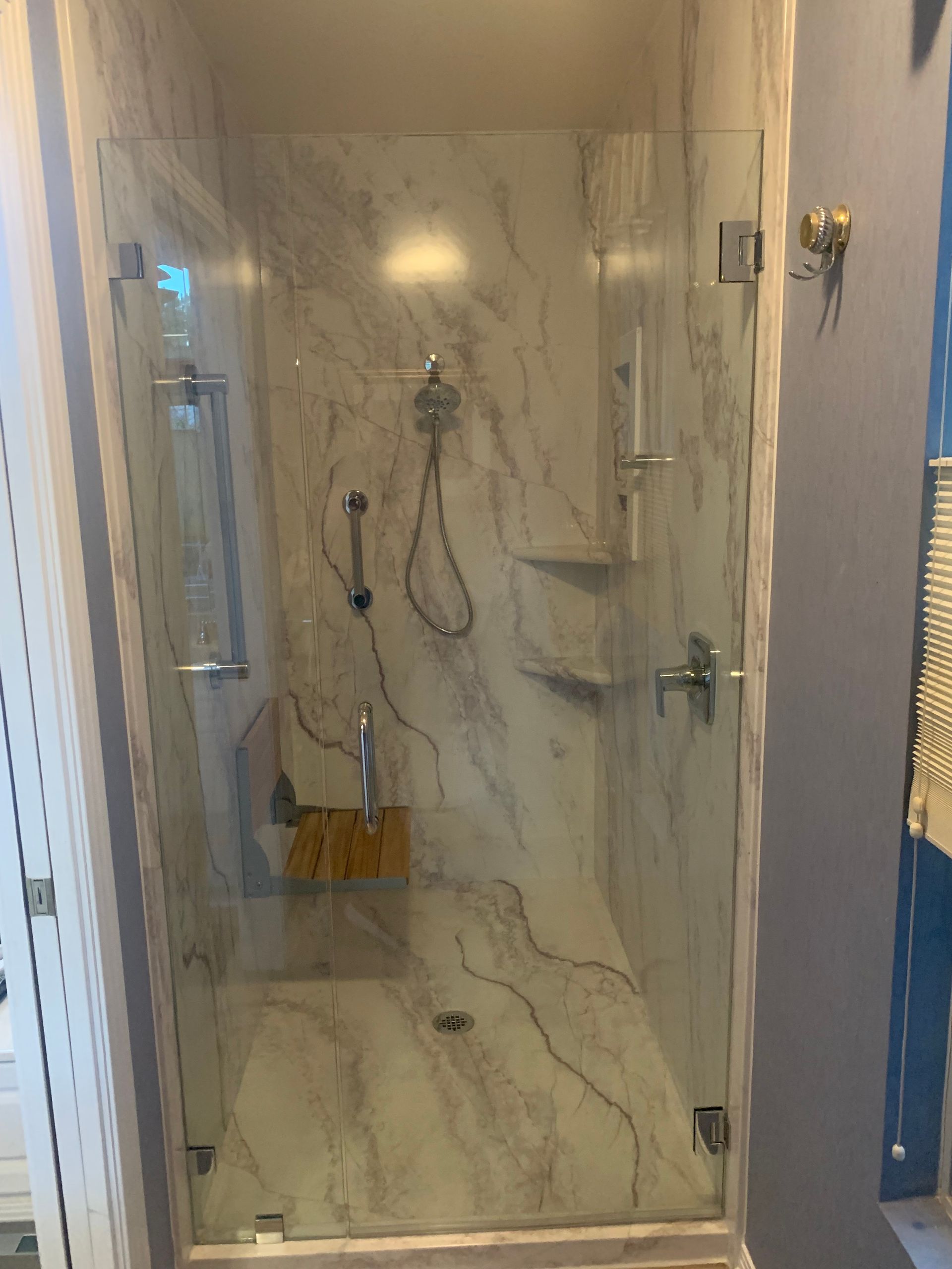 A bathroom with a walk in shower with a glass door and marble walls.