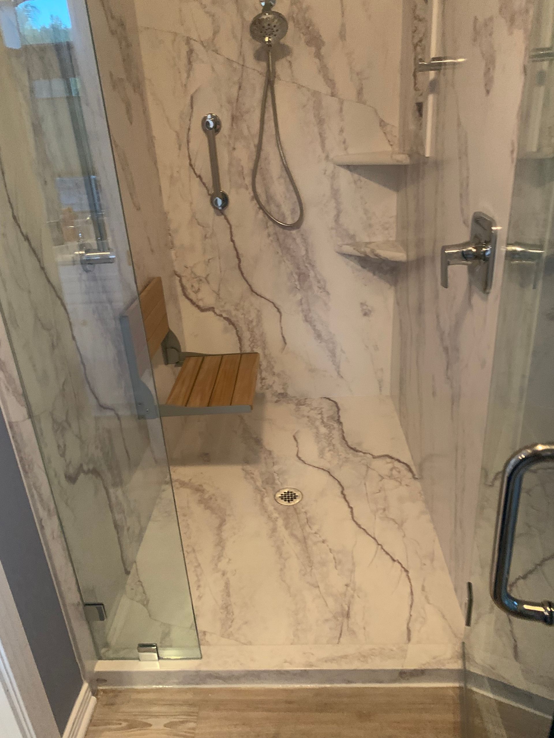 A bathroom with a walk in shower and a wooden bench.