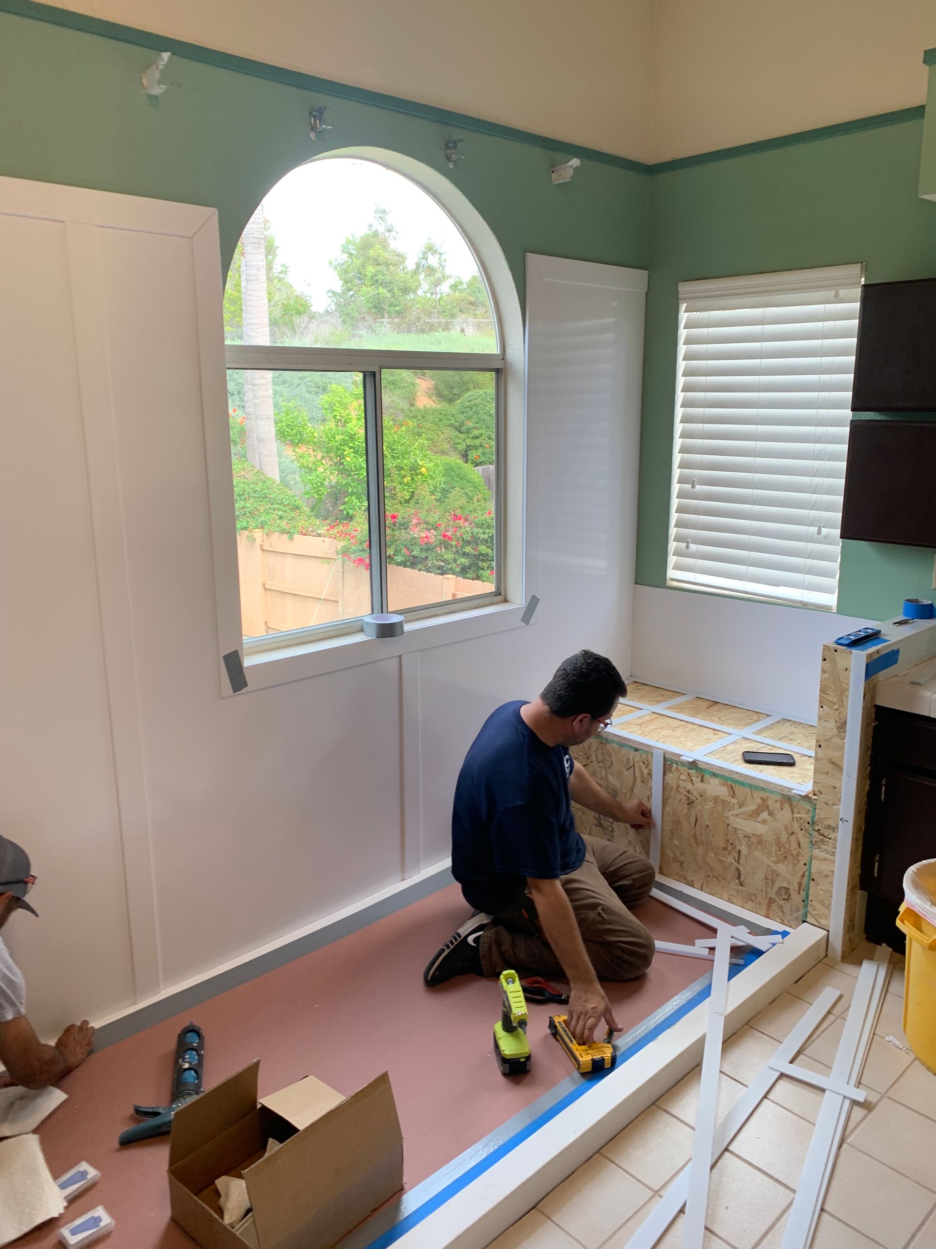 A man is kneeling on the floor in a room with a window.