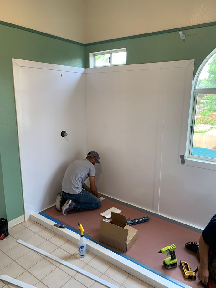 A man is kneeling on the floor in a room while installing a shower stall.