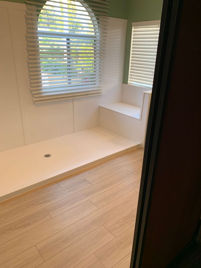 A bathroom with a walk in shower and a window with blinds.