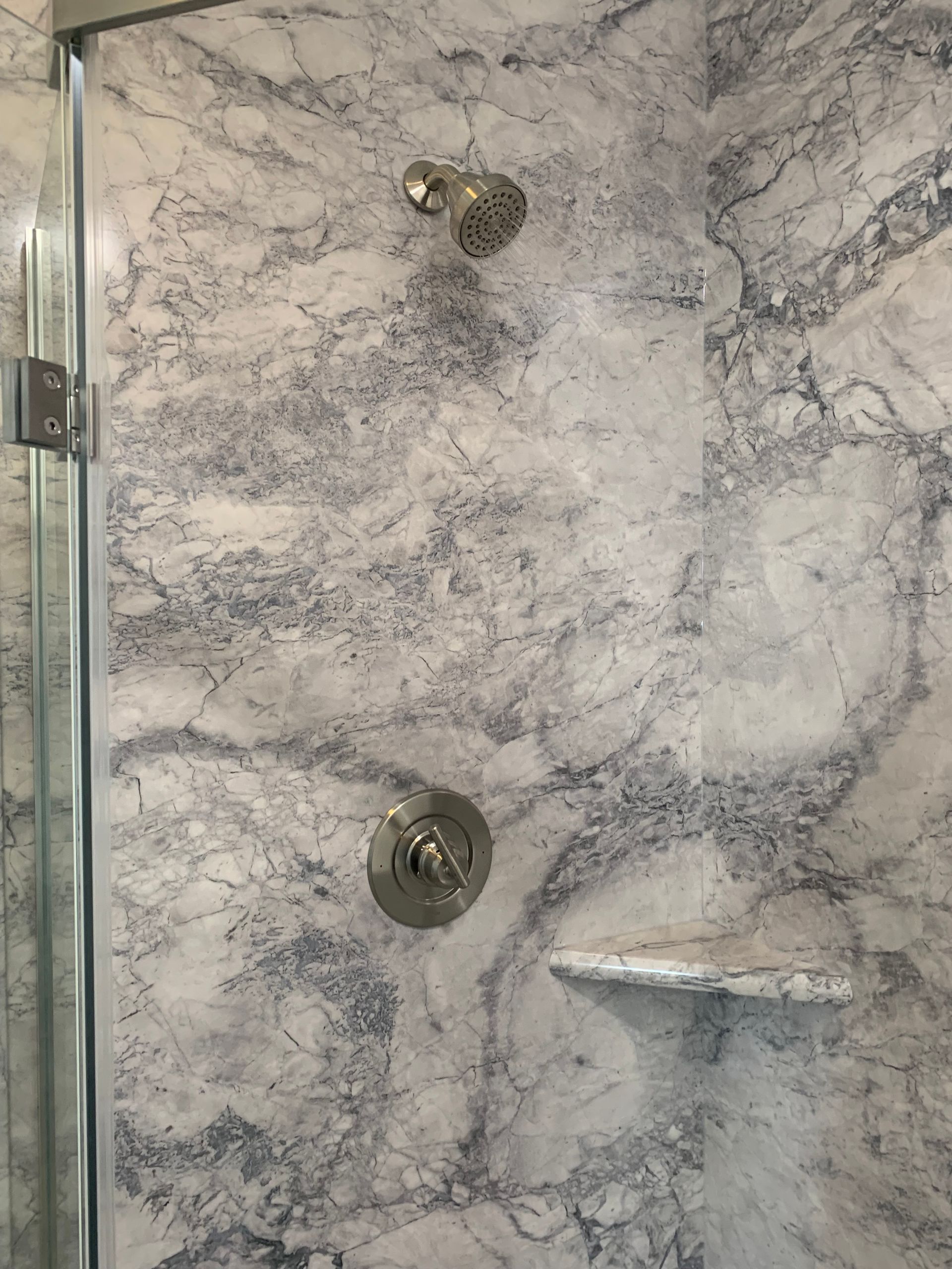 A shower stall with a marble wall and a glass door.