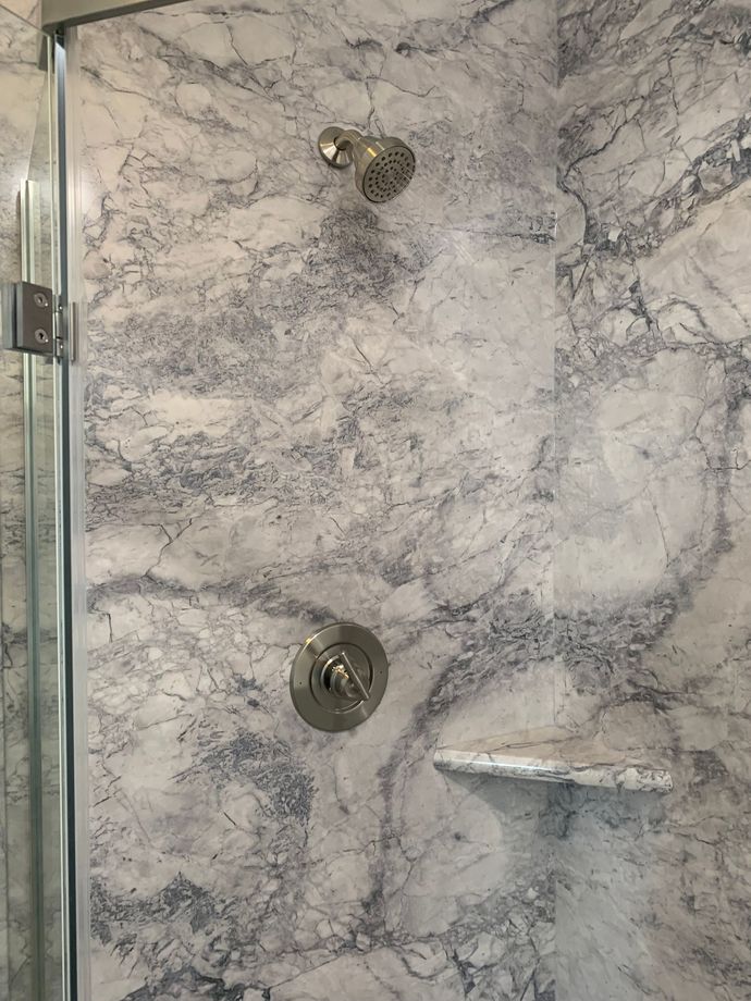 A shower stall with a marble wall and a glass door.