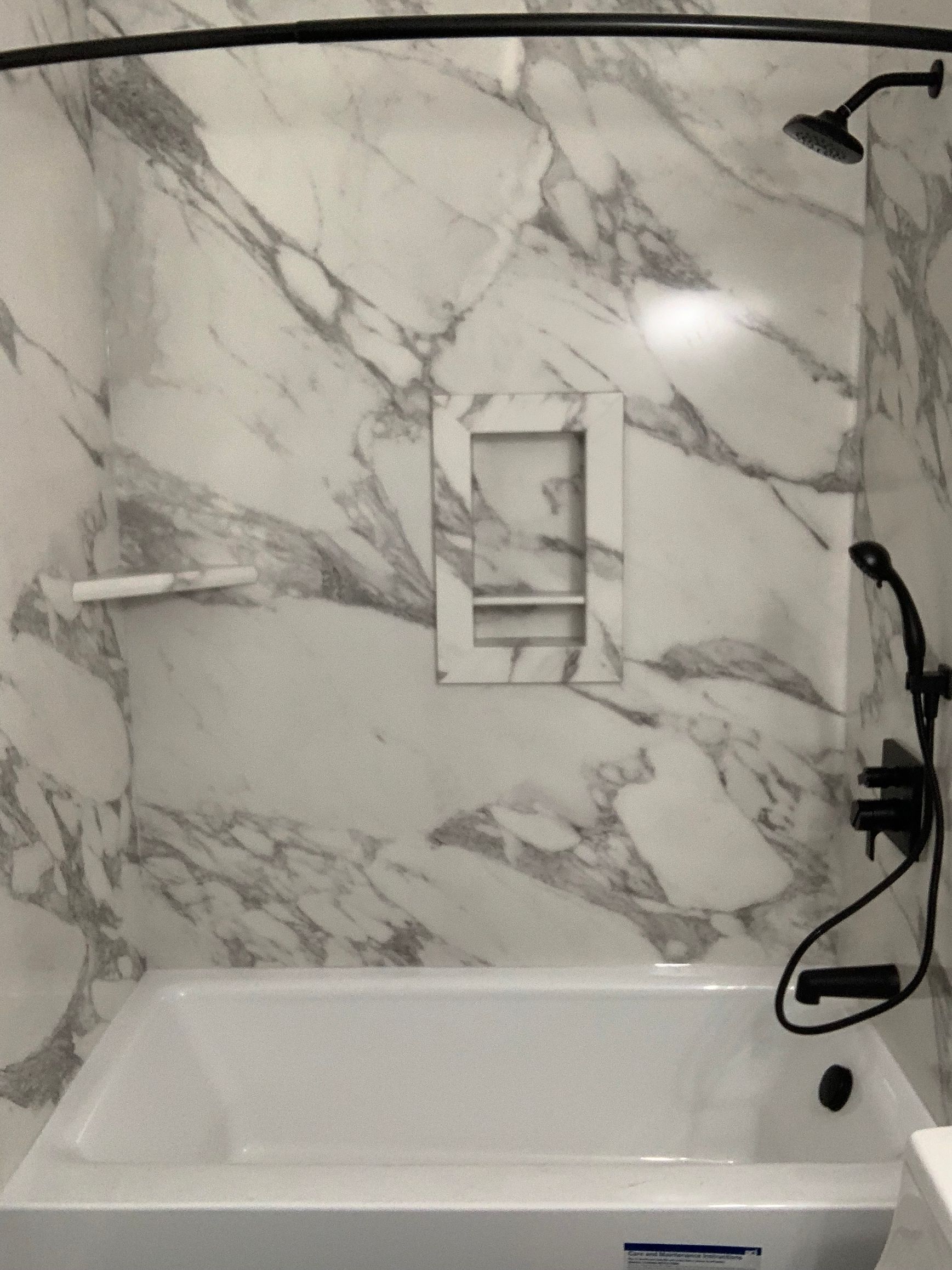 A bathroom with a bathtub , shower , and marble wall.