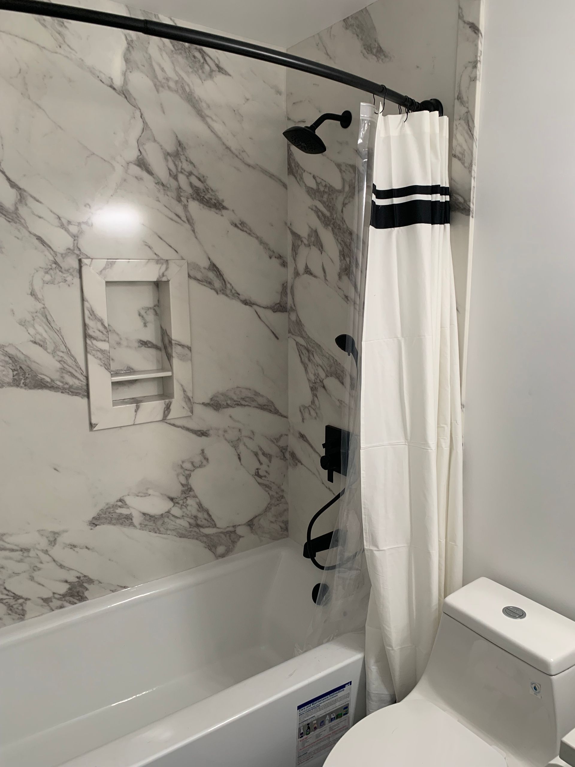 A bathroom with marble walls , a tub , toilet and shower