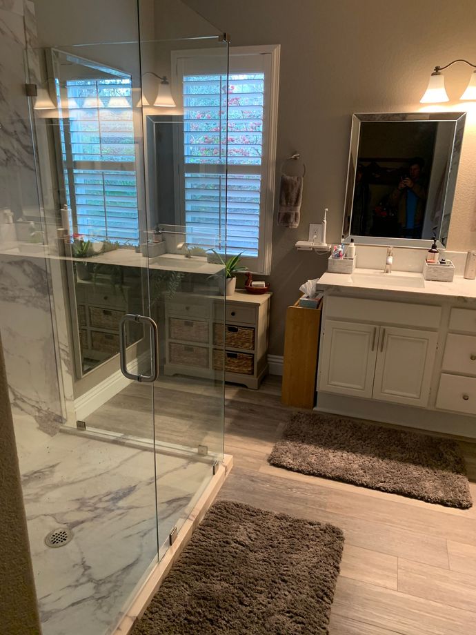 A bathroom with a walk in shower , two sinks , a mirror and a rug.