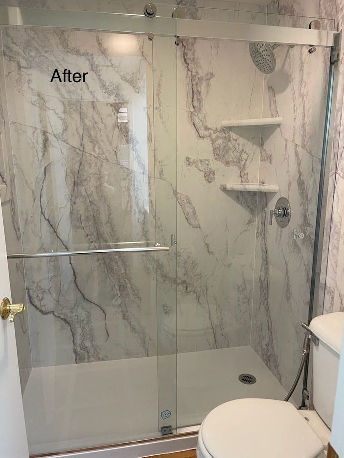 A bathroom with marble walls and a sliding glass shower door.