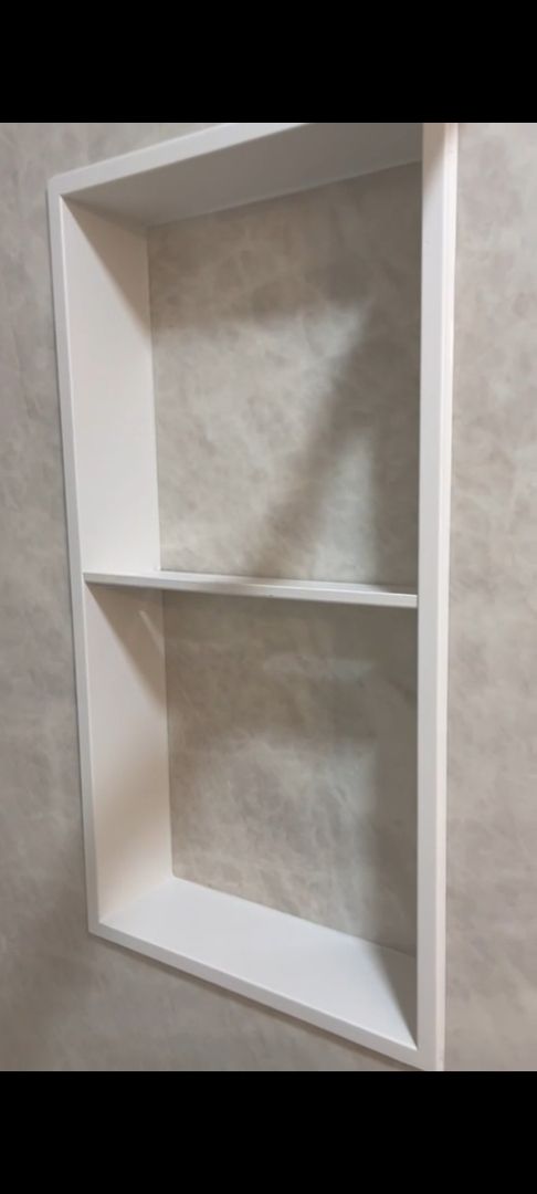 A white shelf is sitting on a gray wall.