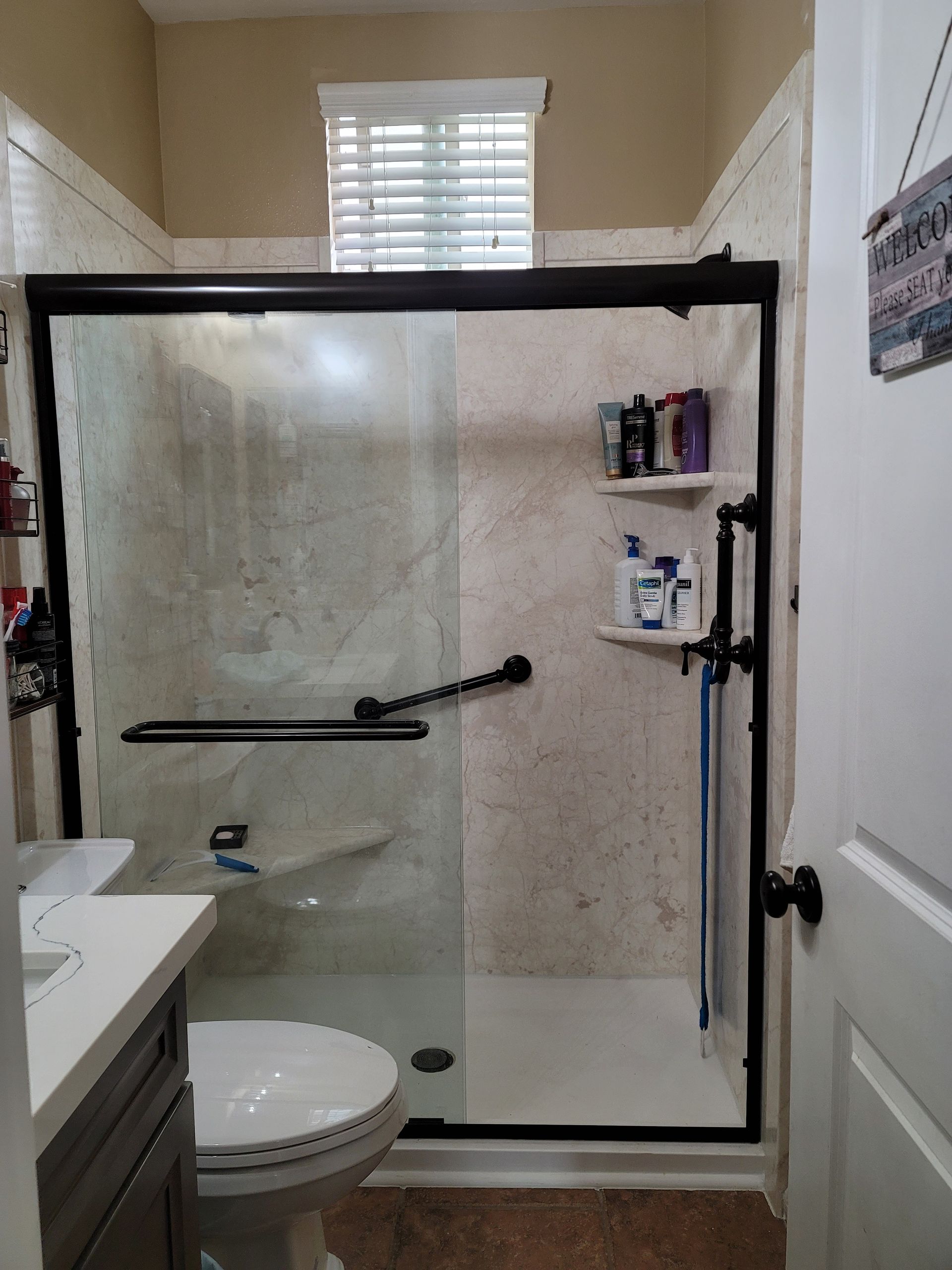 A bathroom with a toilet , sink and shower with a sliding glass door.