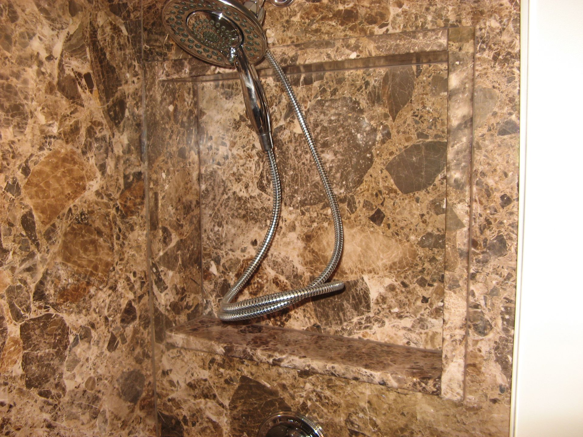 A shower head is hanging from a marble wall.