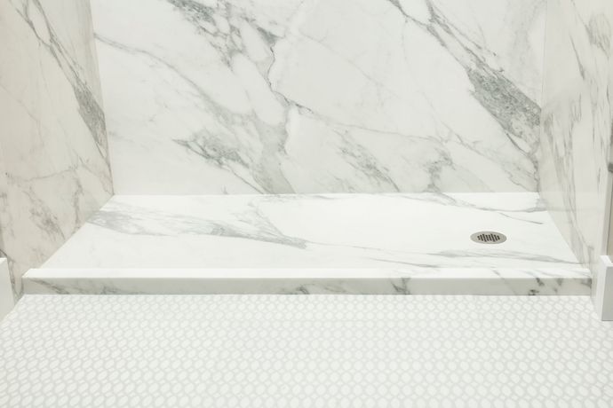 A shower stall with a marble wall and a white tile floor.