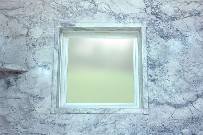 A square window in a marble wall in a bathroom.