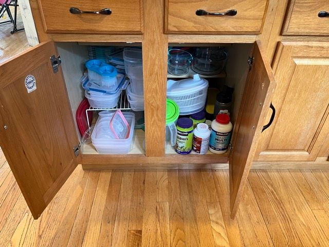 A kitchen cabinet with its doors open and filled with cleaning supplies.