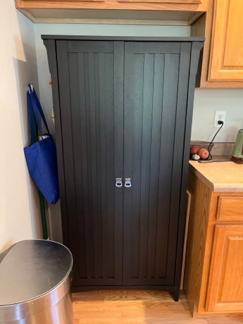 A black cabinet in a kitchen next to a trash can