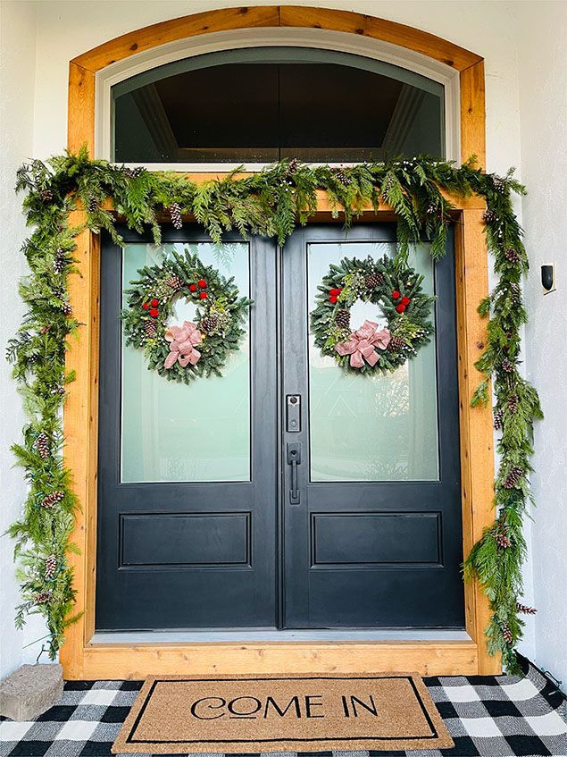 The front door of a house is decorated with christmas wreaths and a welcome mat.