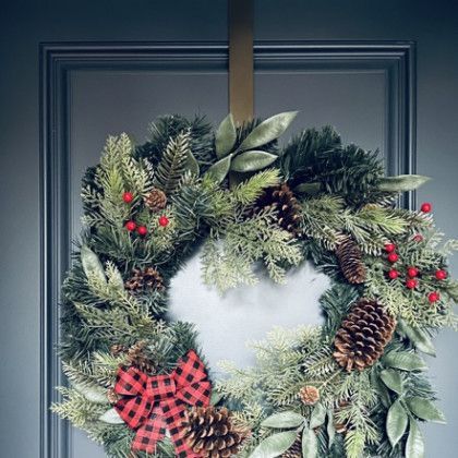 A christmas wreath with pine cones and berries is hanging on a door.
