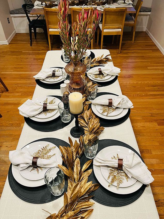 A long table with plates , napkins , candles , and leaves on it.