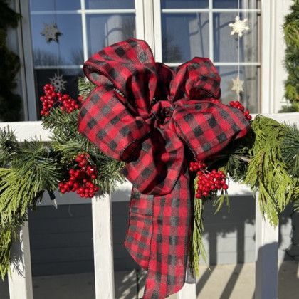 A red and black plaid bow is hanging on a white railing.