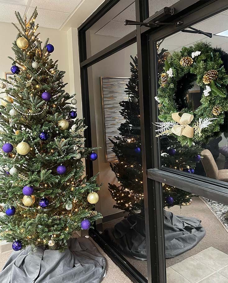 A christmas tree with purple and gold ornaments is in front of a glass door.