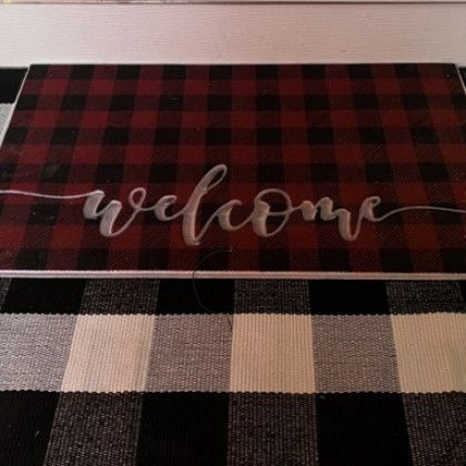 A welcome mat is sitting on top of a black and white checkered rug.