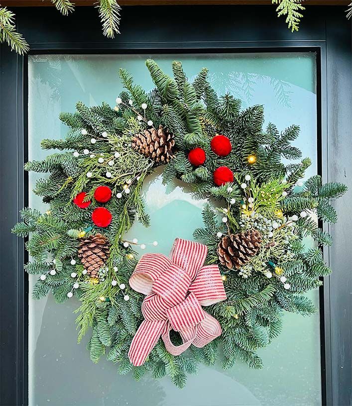 A christmas wreath is hanging on a glass door.
