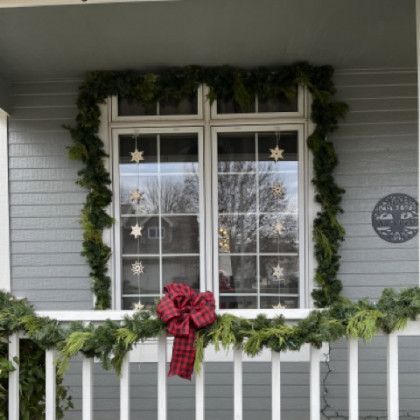 A window on a porch decorated with christmas garland and a red bow.