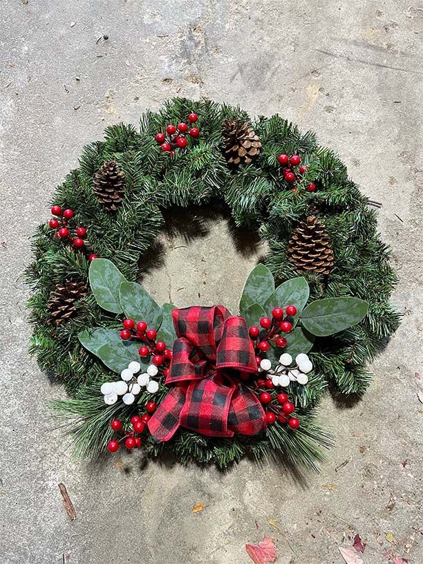 A christmas wreath with red berries , pine cones , and a red and black plaid bow.