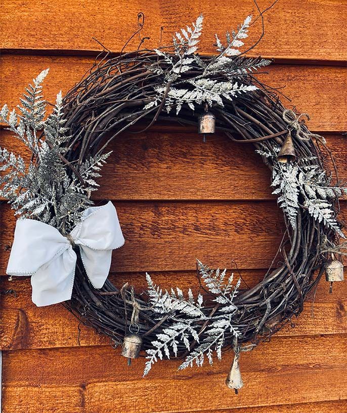A wreath with bells and ferns is hanging on a wooden wall.