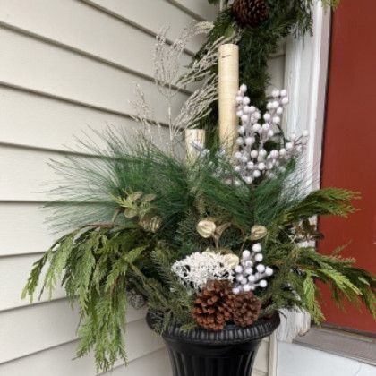 A planter filled with christmas decorations and a candle on a porch.