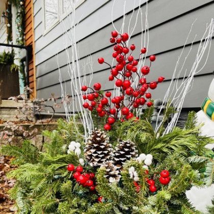 A christmas planter with pine cones and red berries in front of a house