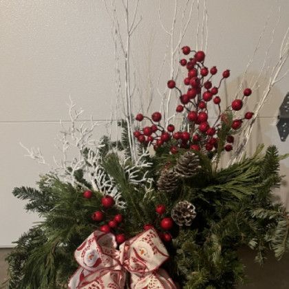 A christmas wreath with red berries , pine cones , and a bow.