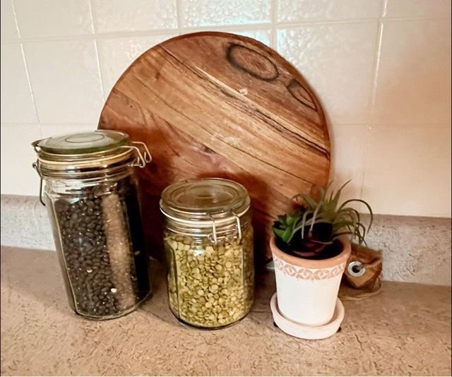 Three jars sitting on a counter next to a cutting board and a potted plant