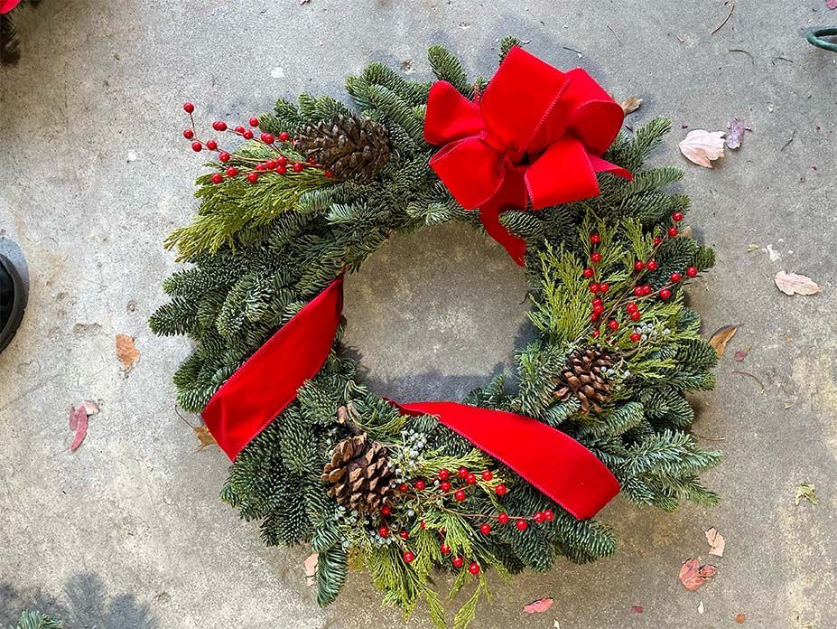A christmas wreath with a red bow is sitting on the ground.