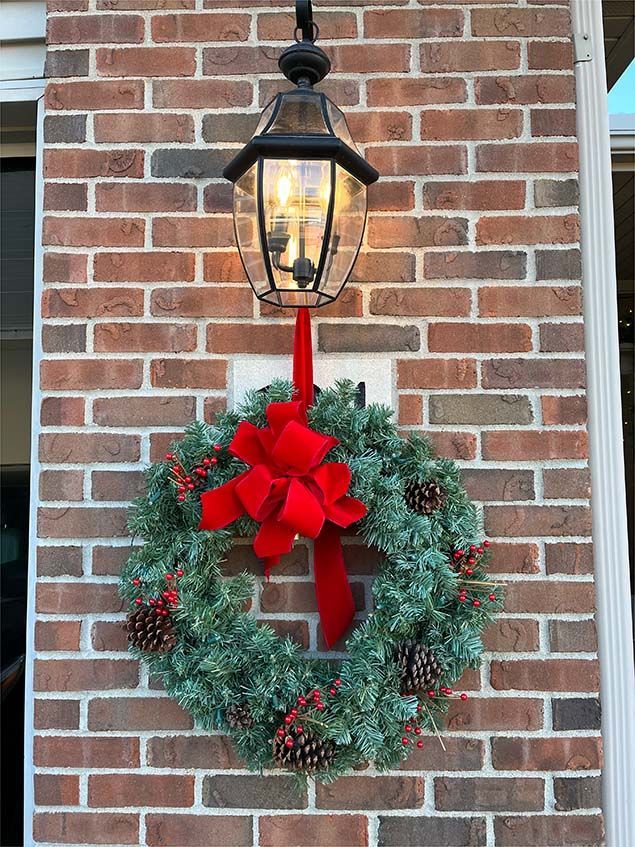 A christmas wreath with a red bow is hanging on a brick wall.