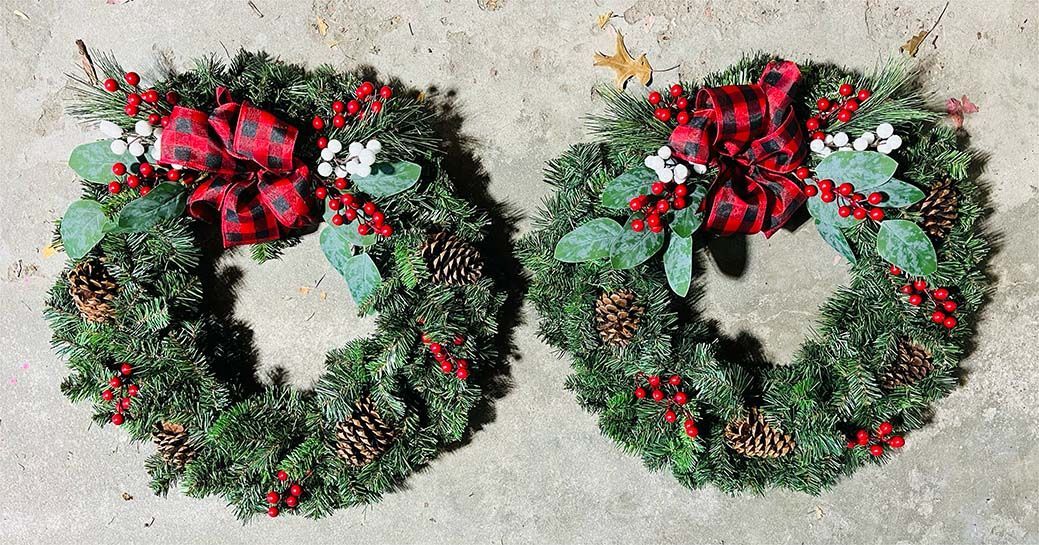 Two christmas wreaths are sitting on a concrete surface.