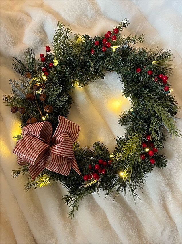 A christmas wreath with red berries and lights is sitting on a white blanket.