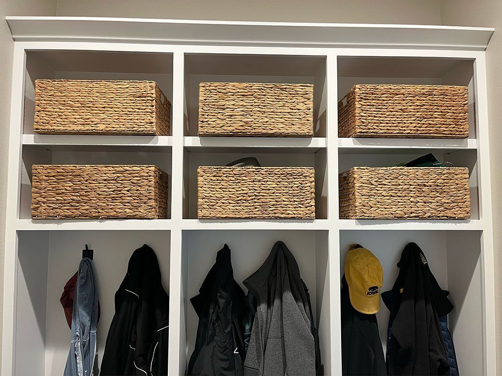 A closet with wicker baskets and coats hanging on hooks.