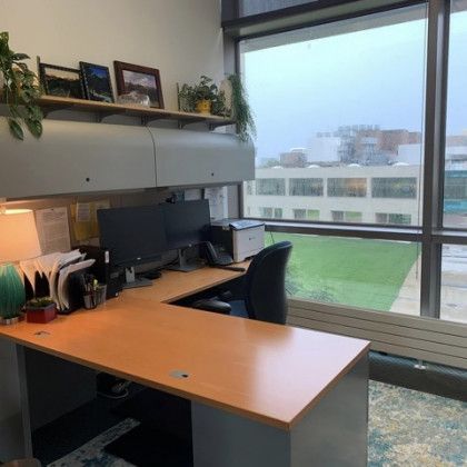 A desk with a computer and a chair in front of a large window.
