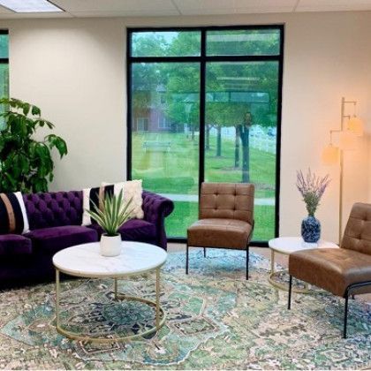 A living room with a purple couch , brown chairs , a coffee table and a large window.