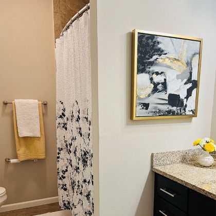 A bathroom with a toilet , sink , shower curtain and a painting on the wall.
