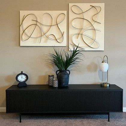 A living room with a black entertainment center , a clock , a lamp , and two paintings on the wall.