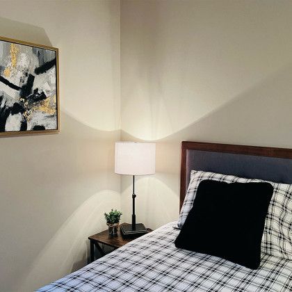 A bedroom with a bed , nightstand , lamp and painting on the wall.