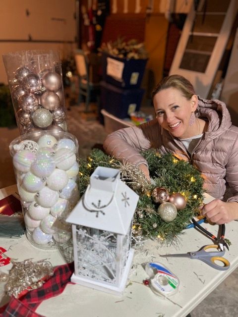A woman is sitting at a table decorating a christmas wreath.