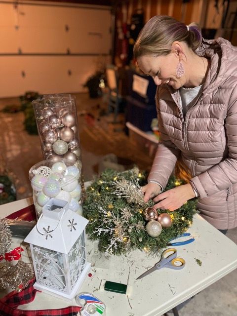 A woman is sitting at a table decorating a christmas wreath.