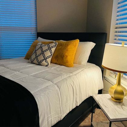 A bedroom with a bed , nightstand , lamp and window.