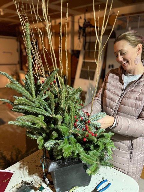 A woman is sitting at a table decorating a christmas tree.