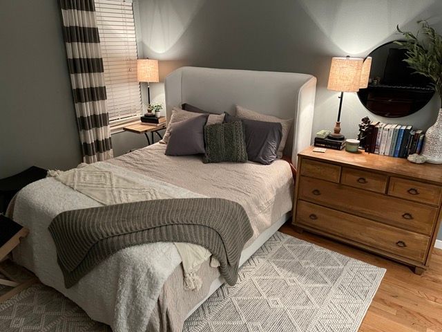 A bedroom with a bed , dresser , lamp and mirror.