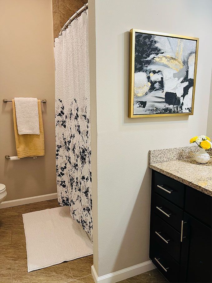 A bathroom with a toilet , sink , shower curtain and a painting on the wall.