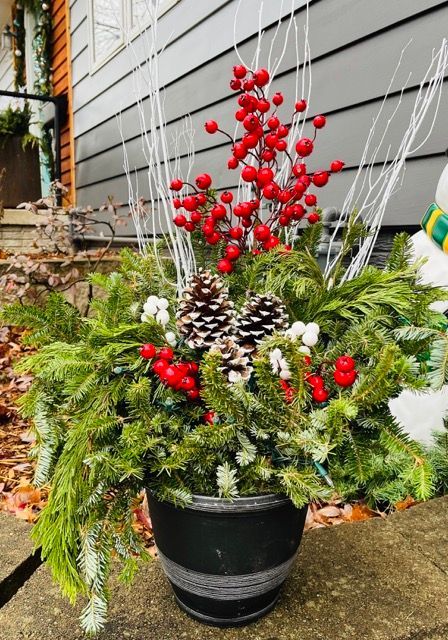 A black pot filled with christmas decorations including pine cones and red berries.
