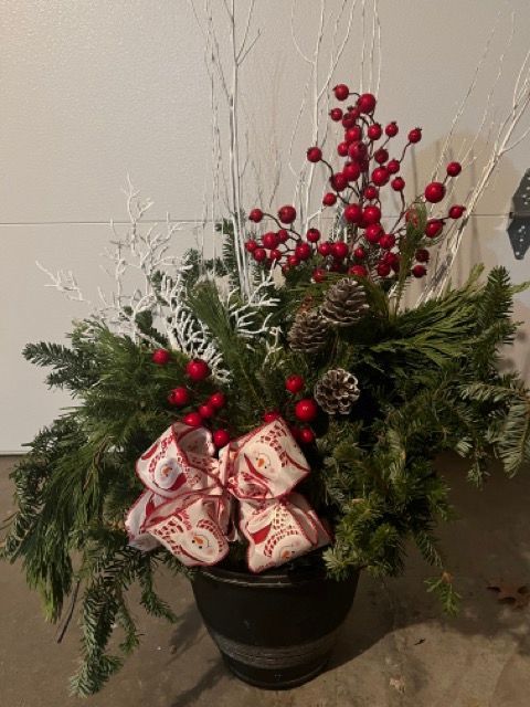 A pot filled with christmas decorations and berries is sitting on the ground.